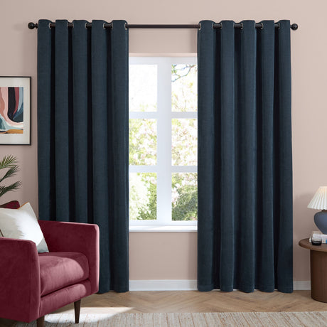 Navy chenille eyelet curtains with grommet headers hung on a dark rod, shown as full-length panels framing a window in a living room with a red armchair.