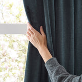 Hand adjusting a navy chenille eyelet curtain by a window, showing the soft matte fabric texture against natural light.