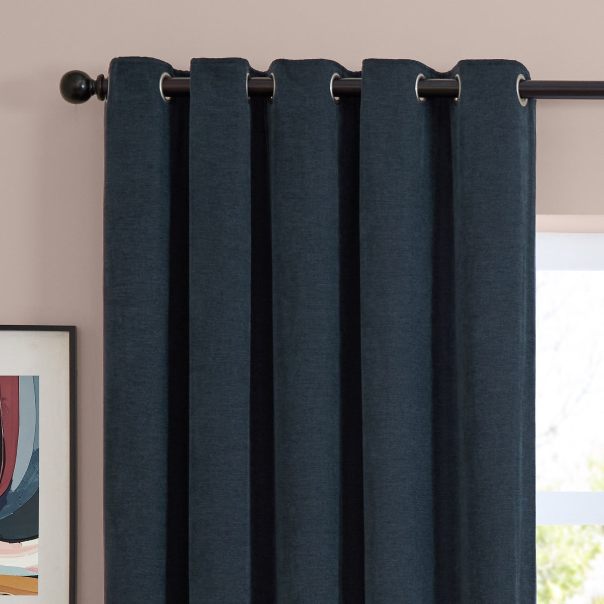 Navy chenille eyelet curtains with silver grommets hung on a dark rod, shown in soft folds against a pink wall near a window.