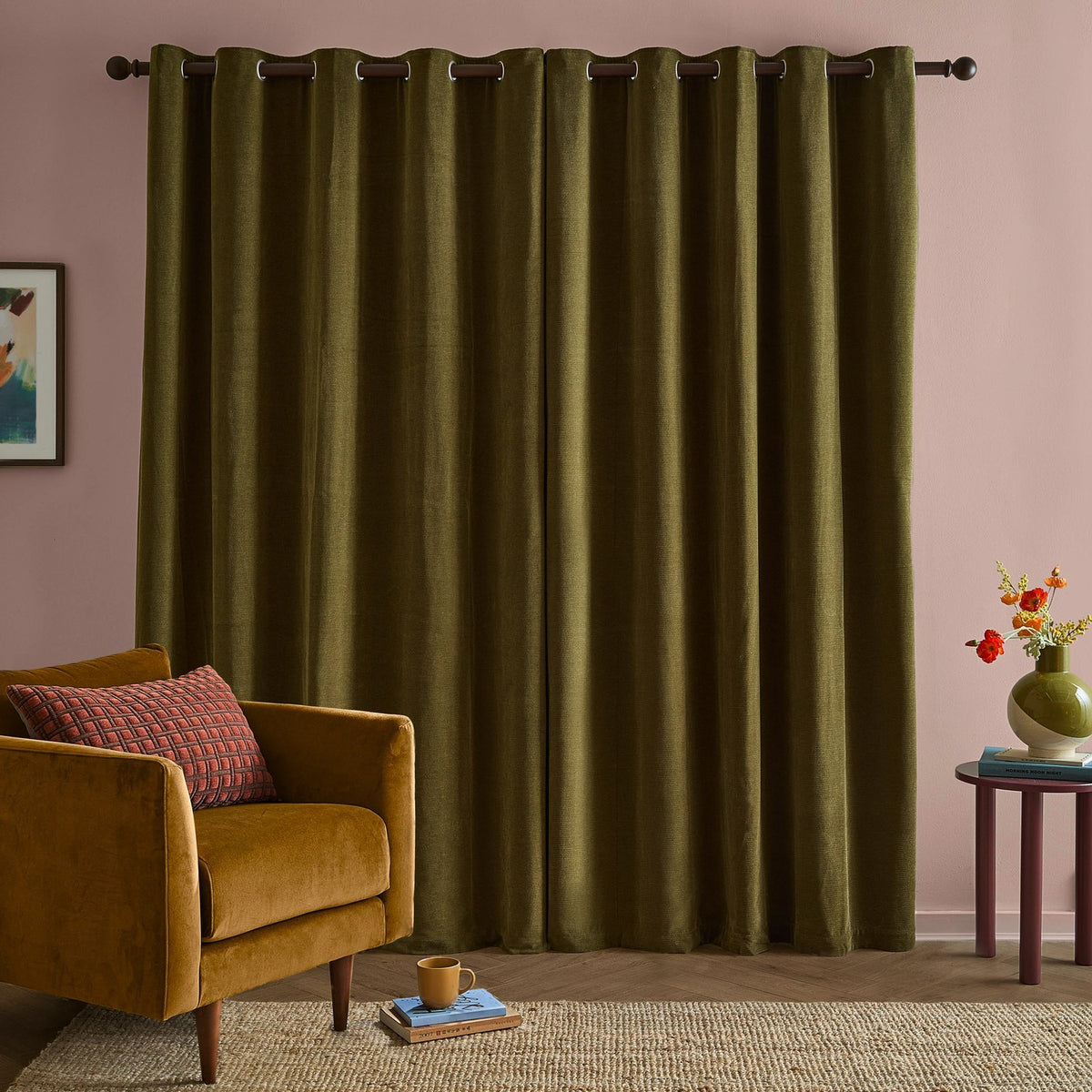 Olive green chenille eyelet curtains with a fully lined, matt finish hanging from a dark rod in a living room with pink walls, styled beside a mustard velvet armchair.