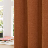 Soft chenille eyelet curtains in rust, shown in deep folds by a bright window with white sill, books, and a candle in the room setting.
