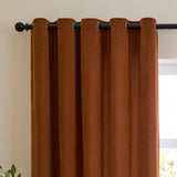 Rust chenille eyelet curtain with metal grommets on a black rod, shown in soft folds against a light wall beside a window.