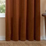 Rust chenille eyelet curtains hanging in soft folds beside a window, shown lined in a living room with a jute rug and wooden side table.