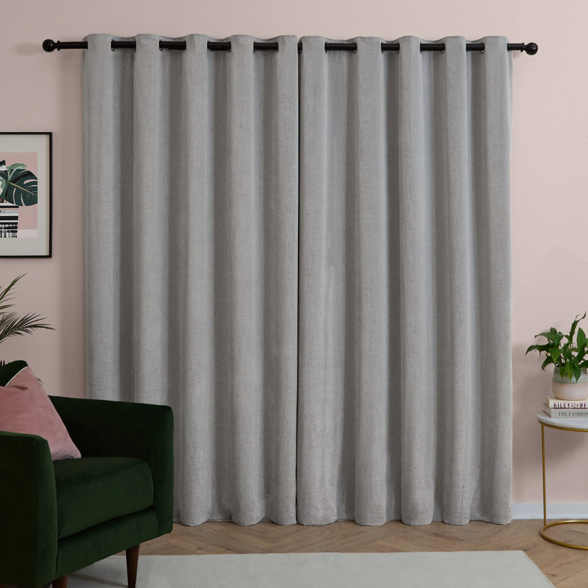 Silver grey chenille eyelet curtains with black rings on a black rod, shown as a lined pair in a living room with pink walls and dark green armchair.