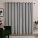Silver grey chenille eyelet curtains with black rings on a black rod, shown as a lined pair in a living room with pink walls and dark green armchair.