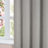 Soft chenille eyelet curtain in silver grey, shown in draped folds beside a window with a light interior setting.