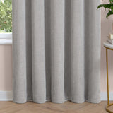 Silver grey chenille eyelet curtain with soft, lined fabric falling in deep folds, shown pooling on a wooden floor beside a window in a living room.