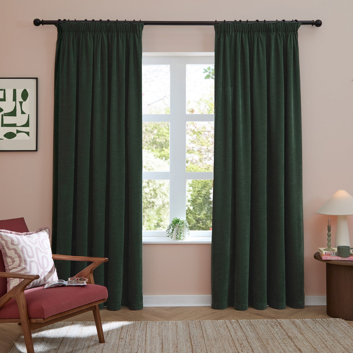 Bottle green chenille pencil pleat curtains with tape heading, shown pair-hung on a black rod either side of a window in a pink living room.