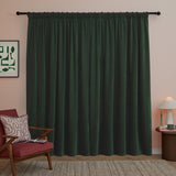 Bottle green chenille pencil pleat curtains with pencil pleat heading on a black pole, styled in a living room with a red armchair and pink wall.