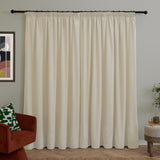 Ecru chenille pencil pleat curtains hung on a black rod in a living room, shown with an armchair, cushion, artwork, and side table.