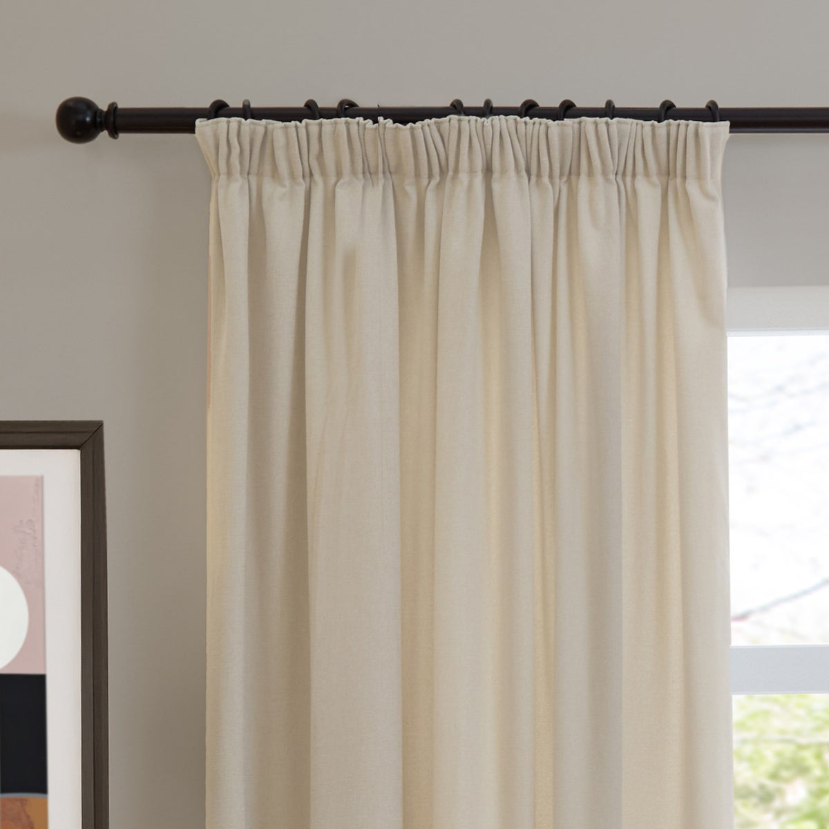 Ecru chenille pencil pleat curtain with gathered heading hung on a dark metal rod, shown in a living room beside a window and framed wall art.