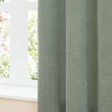 Green pencil pleat curtains in soft chenille fabric with a pencil pleat heading, shown draped beside a window with a light sill and garden view.