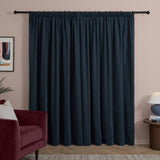 Navy chenille pencil pleat curtains with gathered heading on a black rod, shown in a living room with a burgundy velvet sofa and blush pink wall.