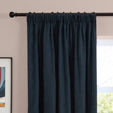 Navy chenille pencil pleat curtains with gathered heading on a black curtain pole, shown against a pink wall beside a window and framed art.