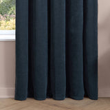 Navy chenille pencil pleat curtains with deep pleated folds, shown hanging by a window in a room with pink walls and wood flooring.