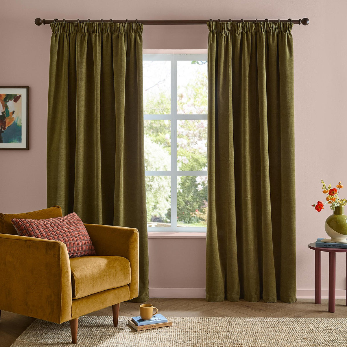 Olive green chenille pencil pleat curtains in matt polyester hang either side of a window in a pink-walled living room with a mustard armchair.