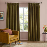 Olive green chenille pencil pleat curtains in matt polyester hang either side of a window in a pink-walled living room with a mustard armchair.