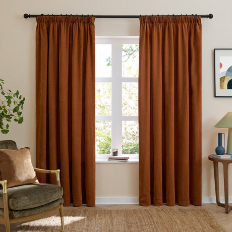 Rust orange pencil pleat curtains in soft chenille fabric, shown hanging on a black rod either side of a window in a living room setting.
