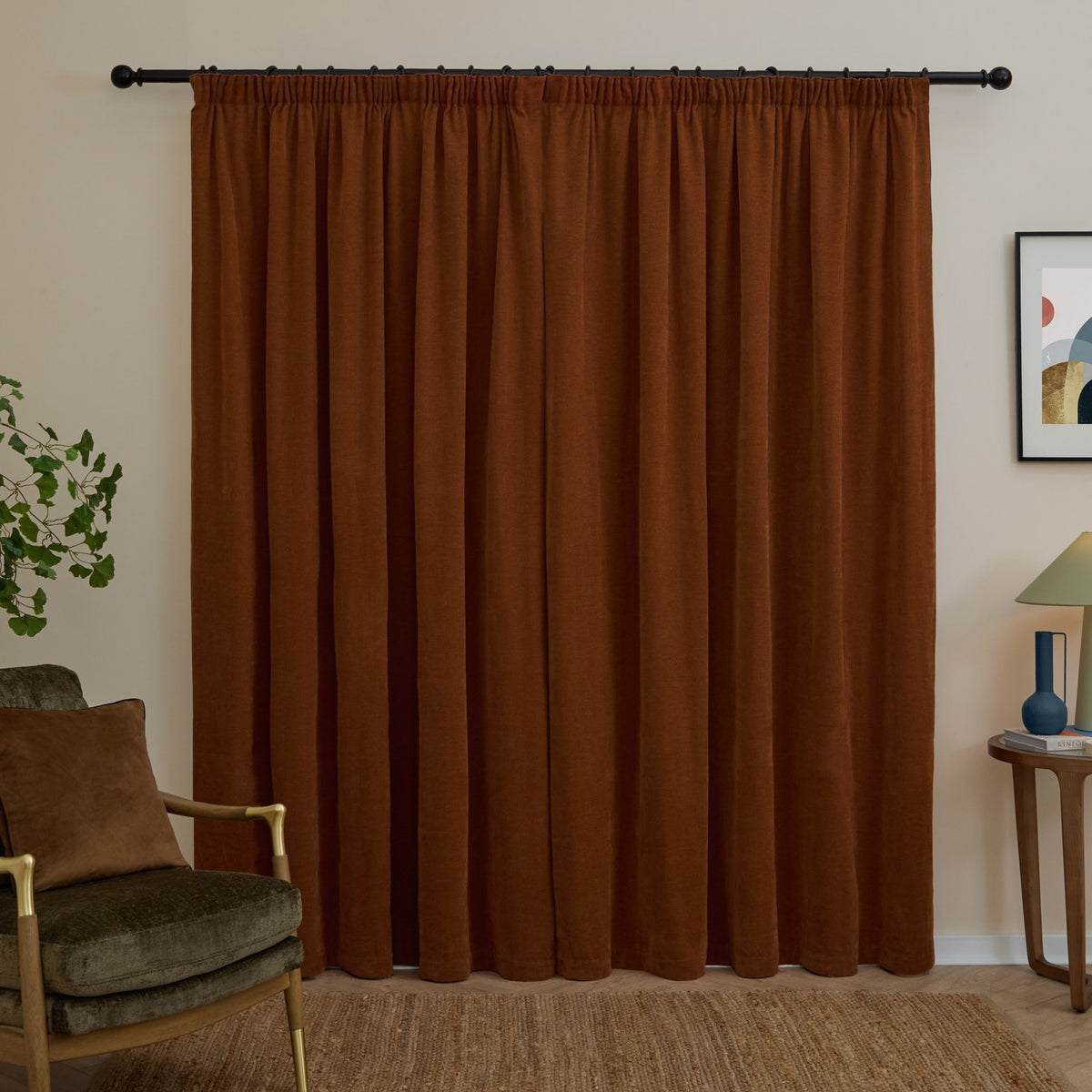 Rust chenille pencil pleat curtains with pencil-pleat heading on a black pole, shown as full-length panels in a living room beside an armchair and side table.