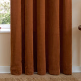 Rust chenille pencil pleat curtains with pencil-pleat heading, shown hanging in soft folds beside a window in a neutral-toned room.