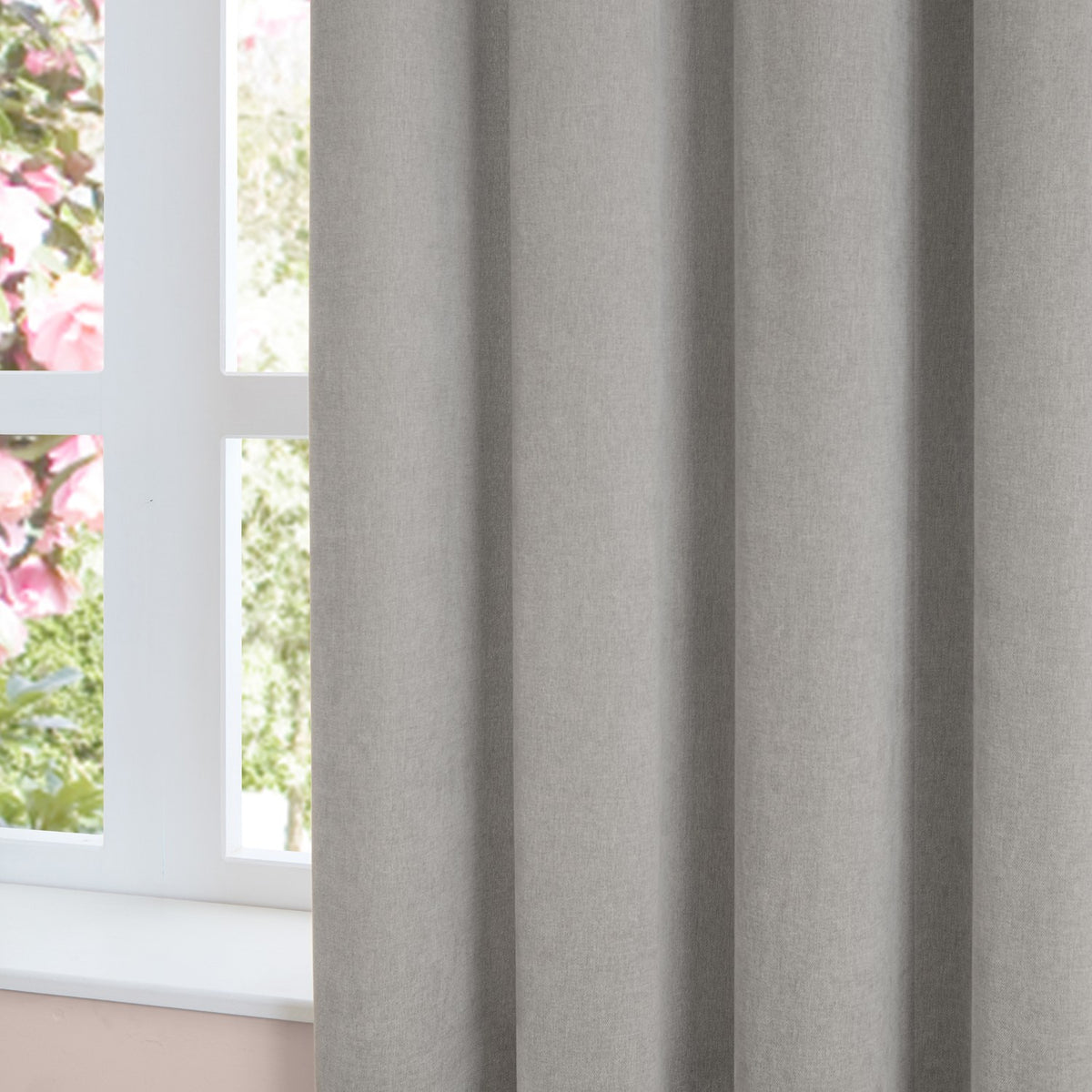 Close-up of silver-grey pencil pleat curtains in soft chenille fabric with a matt, textured finish, shown hanging beside a window with a white frame.