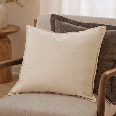 Slub Cotton Plain Linen Cushion in cream, square with flanged edges, shown on a beige armchair with a dark brown patterned cushion behind it.