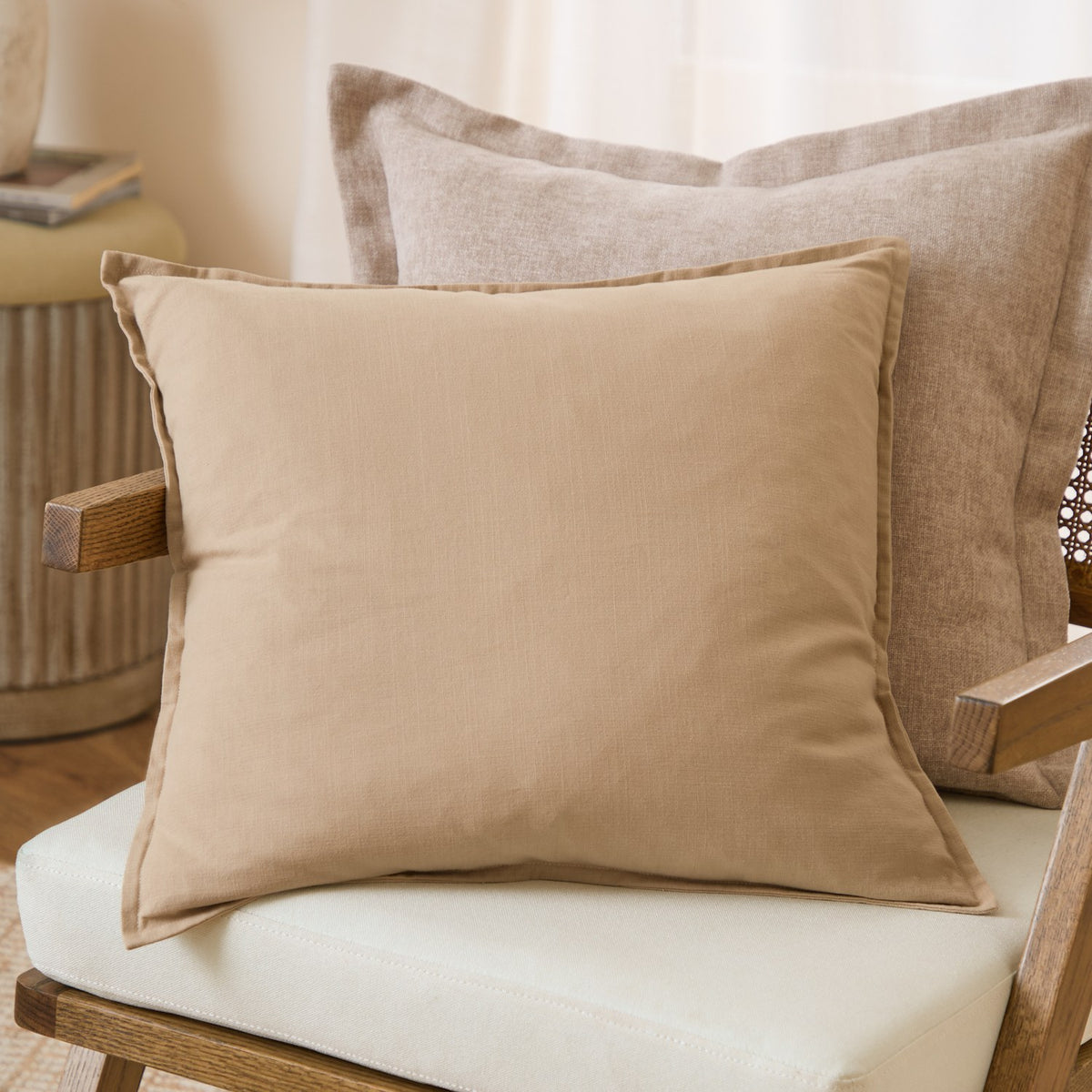 Slub Cotton Woven Plain Cushion in Natural beige with oxford border, shown on a chair against larger textured cushions in a living room setting.