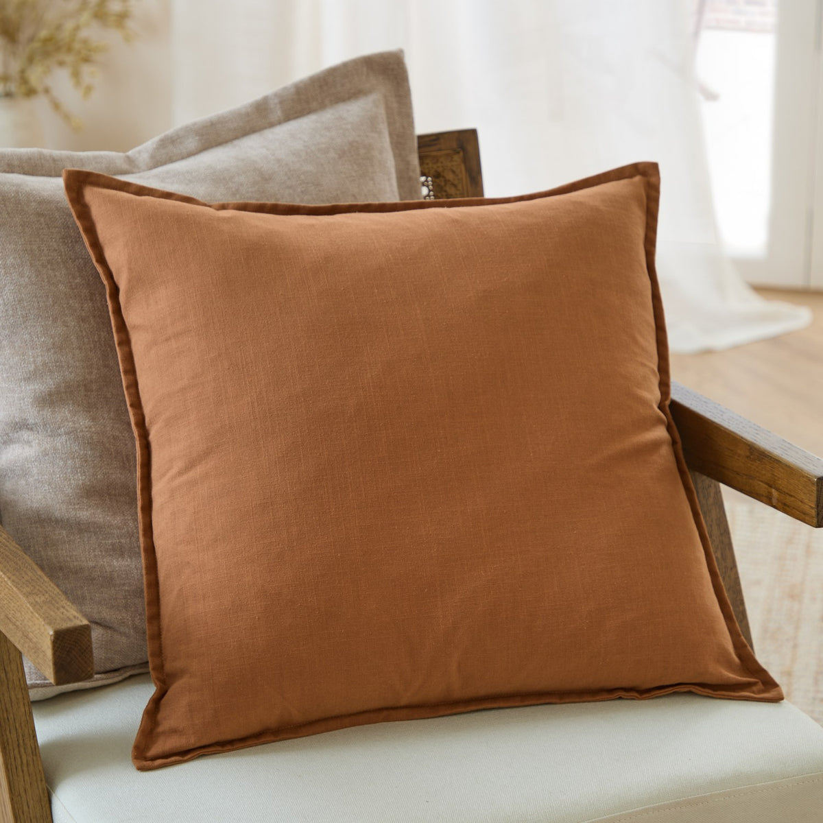 Slub Cotton Woven Plain Cushion in Toffee with an oxford flange border, styled on a neutral armchair beside a linen cushion in a living room setting.