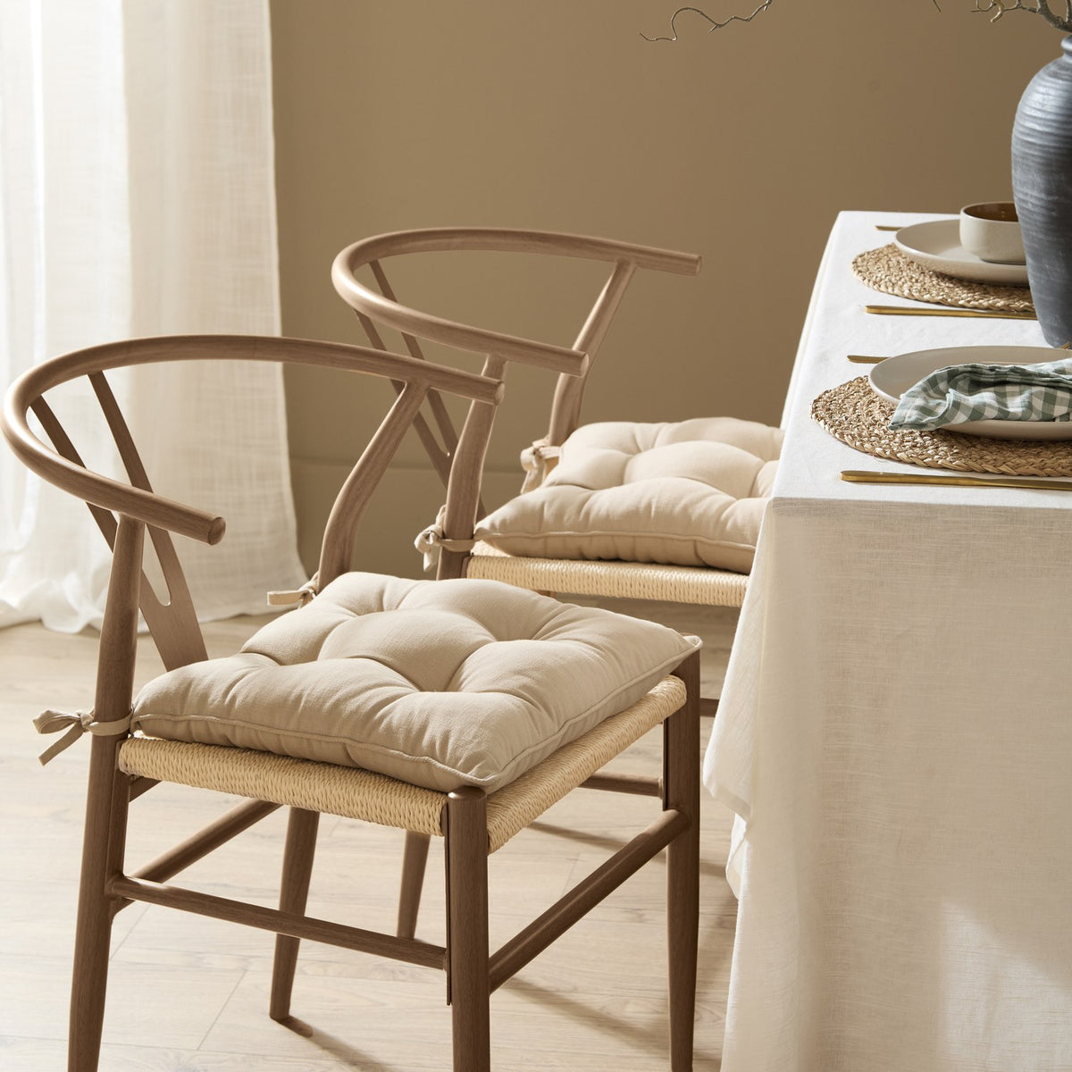 Slub Cotton Plain Linen seat pads in beige on wishbone-style dining chairs with woven rattan seats, tufted with tie fastenings, set beside a linen-covered table.