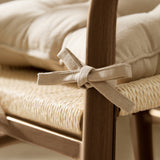 Close-up of a Slub Cotton Plain Linen Seat Pad in beige on a woven wicker chair seat, tied to the wooden frame with fabric ties in a bow.