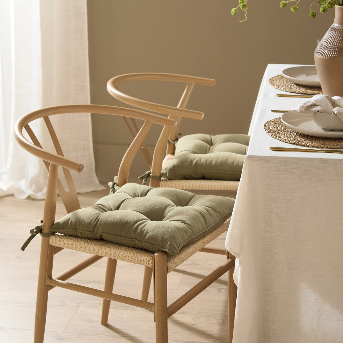 Slub Cotton Plain Polyester Seat Pad in Moss green tied onto wishbone-style dining chairs with woven seats at a set table.