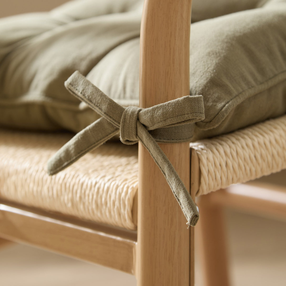 Close-up of a Slub Cotton Seat Pad in moss green tied with fabric ties to a wooden dining chair, showing its slub-textured cotton fabric and plush filling.