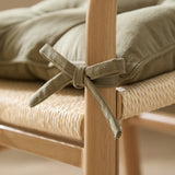 Close-up of a Slub Cotton Seat Pad in moss green tied with fabric ties to a wooden dining chair, showing its slub-textured cotton fabric and plush filling.