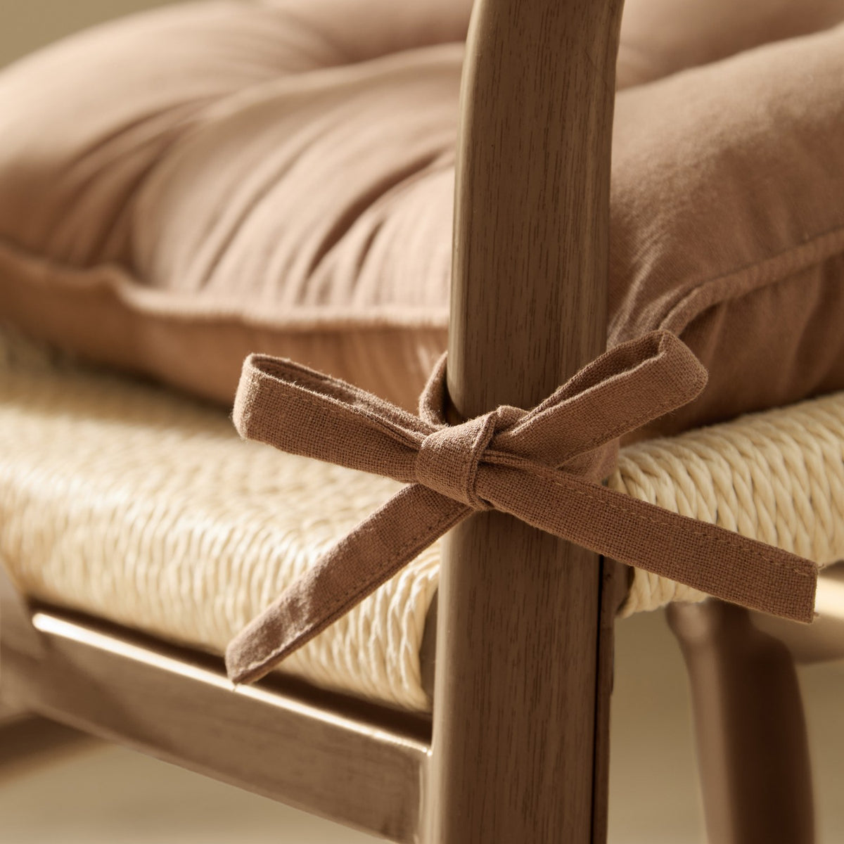 Close-up of a toffee brown slub cotton seat pad tied with fabric ties to a wooden chair leg, shown over a woven seat and cushion.