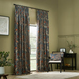 Seaweed Floral Velvet Cushion in indigo on a matching armchair, showing coral-red florals and leaf motifs, in a living room with printed curtains and dark furniture.