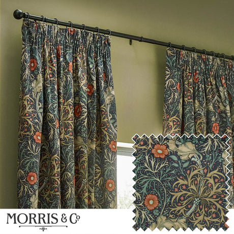 Pencil pleat curtains in indigo velvet with a Seaweed floral pattern in green, sand and coral, shown pleated on a black rod in a living room with olive green walls, plus a fabric swatch detail.