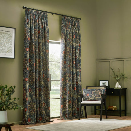 Seaweed pencil pleat curtains in indigo velvet with a trailing floral pattern, pencil pleat heading on a black rod in a living room setting.