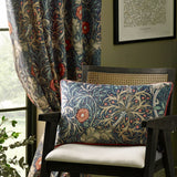 Seaweed fully lined velvet pencil pleat curtain in indigo with a Morris & Co. floral pattern, shown hanging by a window beside a matching printed cushion on a chair.
