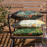 Stack of three Seaweed Floral polyester cushions in forest green, sage and cream, with scrolling foliage and coral blooms, shown on an outdoor bench.