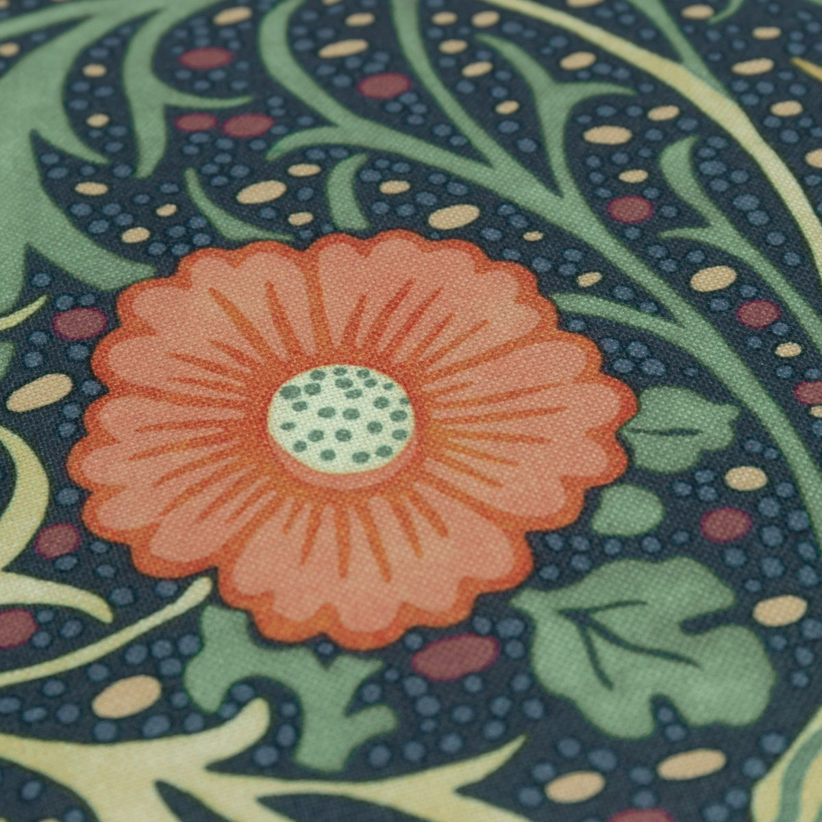 Close-up of the Seaweed Floral polyester cushion in indigo, showing an orange daisy-like flower with dotted centre amid curling green foliage on a dark blue ground.