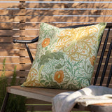 Seaweed Floral polyester cushion in Stone/Sunflower on an outdoor bench, cream ground with sage green foliage, gold florals, orange flowerheads, and piped edge trim.