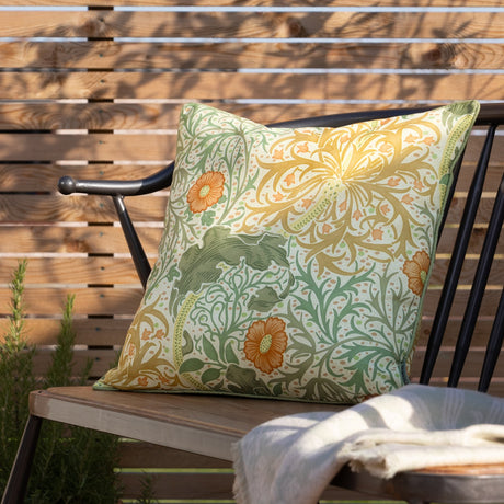 Seaweed Floral polyester cushion in Stone/Sunflower on an outdoor bench, cream ground with sage green foliage, gold florals, orange flowerheads, and piped edge trim.