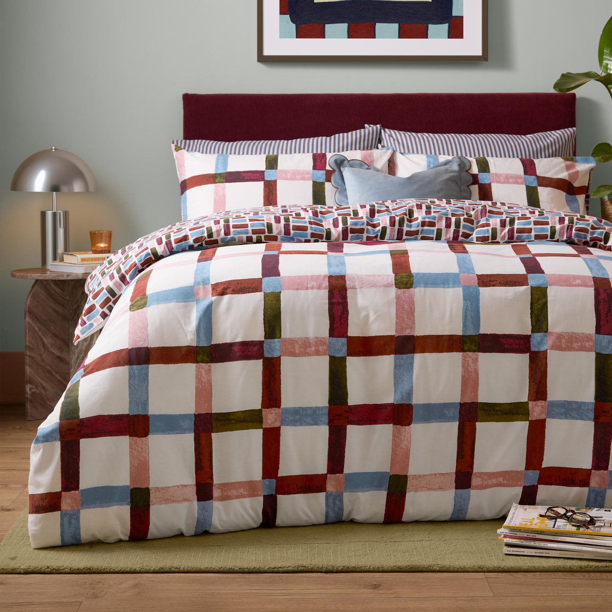 Selvan Reversible Check Duvet Cover Set in Oatmilk & Burgundy, styled on a bed with red, blue, olive and pink check pattern, matching pillowcases and burgundy headboard.