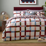 Selvan Reversible Check Duvet Cover Set in Oatmilk & Burgundy, styled on a bed with red, blue, olive and pink check pattern, matching pillowcases and burgundy headboard.