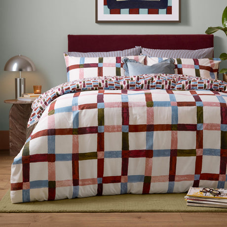 Selvan Reversible Check Duvet Cover Set in Oatmilk & Burgundy, styled on a bed with red, blue, olive and pink check pattern, matching pillowcases and burgundy headboard.