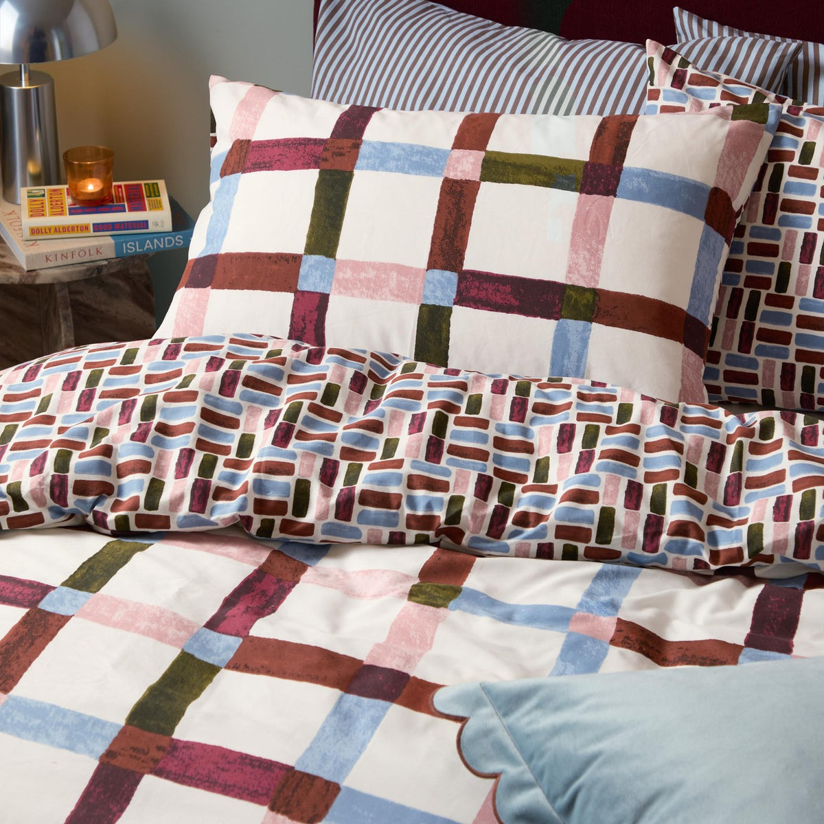 Selvan Reversible Check Duvet Cover Set in Oatmilk & Burgundy, styled on a bed with matching pillowcases showing both the check and tile prints in red, blue, olive and pink.