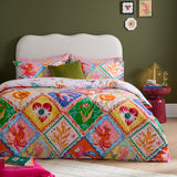 Seraphine Reversible Abstract Duvet Cover Set in Multi, shown on a bed with matching pillowcases in a geometric diamond print featuring mythical creatures in orange, pink, green, blue and yellow.