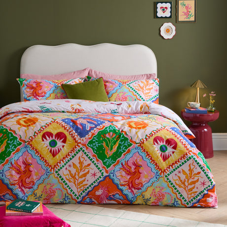 Seraphine Reversible Abstract Duvet Cover Set in Multi, shown on a bed with matching pillowcases in a geometric diamond print featuring mythical creatures in orange, pink, green, blue and yellow.