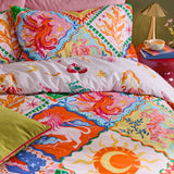 Seraphine Reversible Abstract Duvet Cover Set in Multi, shown on a bed with patchwork diamond motifs of phoenixes, suns and stars in orange, pink, blue and yellow, styled in a bedroom setting.