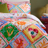 Seraphine Reversible Abstract Duvet Cover Set in Multi, shown on a bed with geometric diamond patchwork featuring mythical creatures, hearts, suns and florals in orange, pink, green and blue tones.